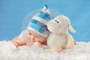 Cmile baby in hat, hugging toy on a white bedspread, on a blue b