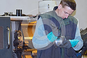 CNC-machinist at work. He checks metal part which was already produced by the machine.