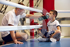 Coach assist to little athlete. Beginner boxer in sport uniform drinking water after workout at sports gym. Concept of