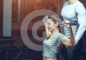 The coach helps a young athlete perform an exercise lifting dumbbells with a sports hall.