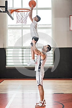 A coach holding a boy on his sholders while he throwing the ball into the ring