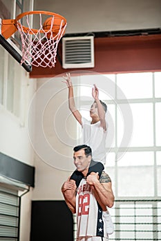 A coach holding a boy on his sholders while he throwing the ball into the ring