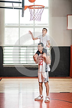 A coach holding a boy on his sholders while he throwing the ball into the ring