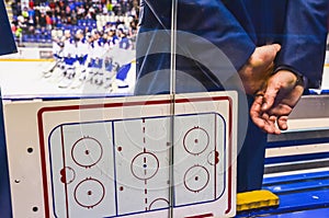 Trenér na lavičce ledního hokeje s taktickou deskou při pohledu na hráče po hokejovém zápase