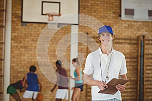 Coach smiling at camera while high school team playing basketball in background