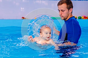 Coach teaches the baby to swim in the pool. baby splash in the water in the pool. The concept of a healthy