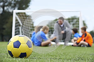 Coach And Team Discussing Soccer Tactics With Ball In Foregroun photo