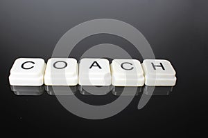 Coach text word title caption label cover backdrop background. Alphabet letter toy blocks on black reflective background. White al