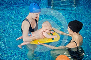 Coach training newborn child floating at swimming courses mom and baby. Women focusing on little child on swimming board