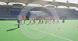 Coach watching female hockey players exercising on the field