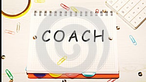 COACH word on a checkered notebook on a light table next to a magnifying glass, paper clips, stationery buttons, a calculator