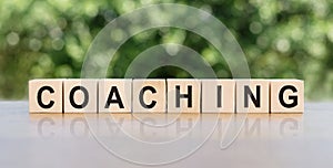 COACHING. Word written on wooden blocks. The text is written in black letters and is reflected in the mirror surface of the table
