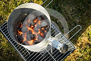 Coal of charcoal grill burning in flames with fire and lighter in barbecue chimney for BBQ evening