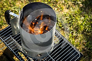 Coal of charcoal grill burning in flames with fire and lighter in barbecue chimney for BBQ evening