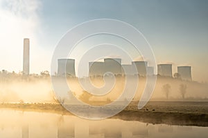 Coal fired electric power station with chimneys and cooling towers surrounded by fog and mist at sunrise next to river haze photo