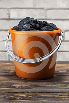Coal pieces in the bucket on brick wall background.