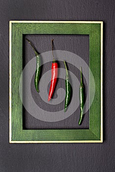 A coalition of red and green: a tangy pair of fresh chili pods against a black background in a portrait frame. Table top view,