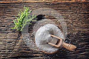 Coarse-grained salt with rosemary herbs in a wooden bowl with a ladle on an old oak table