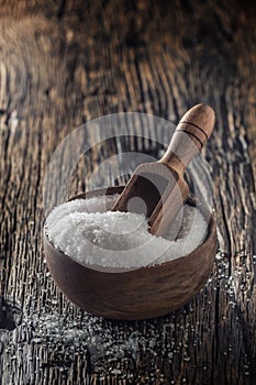 Coarse-grained salt in a wooden bowl with a ladle on an old oak table