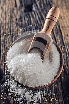 Coarse-grained salt in a wooden bowl with a ladle on an old oak table