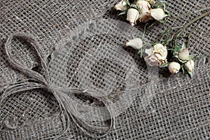 Coarse linen fabric. On it are dried beige roses and a bow of linen threads