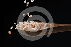 Coarse pink salt dropping on wooden spoon
