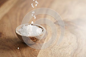 Coarse sea salt falling into wooden bowl on table