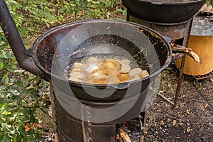 Coarsely chopped potatoes are fried in boiling oil in a cast-iron cauldron on a wood-burning stove.