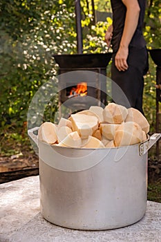 Coarsely chopped potatoes for frying in a cast iron cauldron against the backdrop of an oven with burning wood.