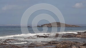 Coast of the atlantic ocean with rocks in the sea, waves,blue sky with clouds,grass in foreground, during sunset