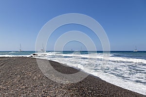 Coast and beach of Vlychada on Santorini island in Greece. In the background blue sky and waves at sea