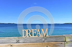 Coast with Dream wooden sign on a handrail. Blue sea, sunny day. Rias Baixas, Spain.