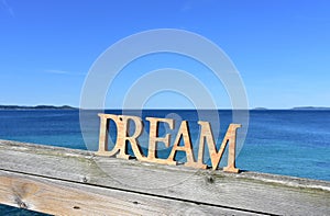 Coast with Dream wooden sign on a handrail. Blue sea, sunny day. Rias Baixas, Spain.