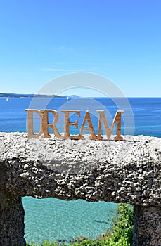 Coast with Dream wooden sign on a handrail. Blue sea, sunny day. Rias Baixas, Spain.