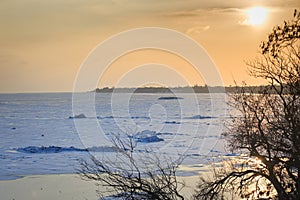 Coast of the frozen sea in winter, ice hummocks, reflection in the water of sun rays at sunset