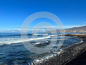 The coast of Las Americas, volcanic beach, blue sky and ocean waves on a sunny October day, Tenerife, Canary Islands, Spain