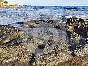 The coast of the Mediterranean Sea, long frozen lava, in the recesses of which there is sea water against a blue sky