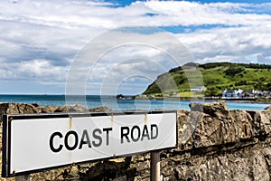 Coast road sign along the Antrim coast road A2 Road in Northern Ireland. Vibrant green landscape and dramatic sky.