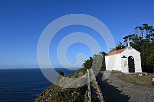 the coast side of a white chapel overlooking water and trees