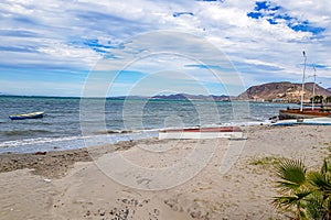 Coastal beach landscape, overturned boat on sand, another in waters