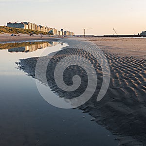 Coastal houses reflecting on a puddle on a sandy beach at sunset in Blankenberge, Belgium