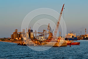 Coastal industrial factory with cranes and structures with port and transport ship. Generic view of industrial harbor with vessels