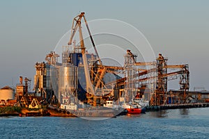 Coastal industrial factory with cranes and structures with port and transport ship. Generic view of industrial harbor with vessels