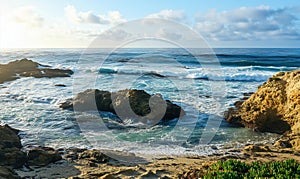 Coastal landscape with waves crashing on rocks, serene ocean view, golden sunlight illuminating water, blue sky with photo