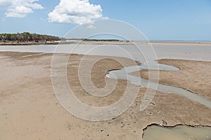 Coastal mudflat at low tide with water running through and blue sky