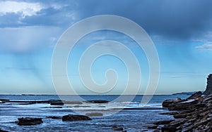 Coastal Rain falling over the ocean against blue sky with seaside rock ledge