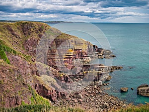 Coastal red cliffs near Manorbier in Pembrokeshire, Wales, UK - the vertically inclined rock strata of the bedrock is of the