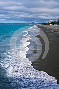 Coastal scenery with calm ocean and tame waves breaking gently over black sand beach under stormy sky. Napier Marine