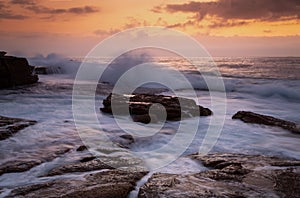 Coastal sunrise waves crashing onto rocks