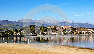 Coastal village reflected in water, with fishing boats and mountains on the background